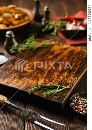 Empty wooden cutting board on kitchen table surrounded with seasonings 117168424