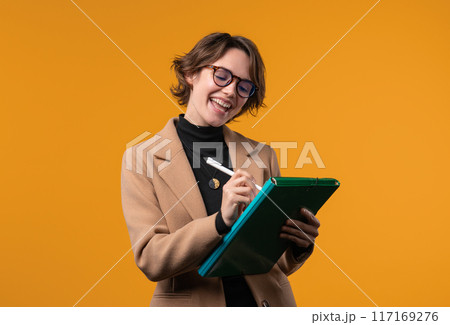 Businesswoman or female student writing notes with pen. Smart lady thinking, about future plans and to-do list in notebook for week, month, year. Keeping personal diary on yellow background Businesswoman or female student writing notes with pen. Smart lady thinking, about future plans and to-do list in notebook for week, month, year. Keeping personal diary on yellow background 117169276