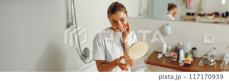 Young beautiful lady looking at her face in a small round mirror doing routine skincare procedures Young beautiful lady looking at her face in a small round mirror doing routine skincare procedures 117170939