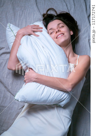 Girl hugs a white soft pillow and wants to sleep. Girl hugs a white soft pillow and wants to sleep. 117172741