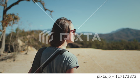 A young woman, wearing sunglasses and a blue shirt, walks along a sandy path on a tropical island. Lush foliage and mountains are visible in the distance. Pai Canyon Chiang Mai , Thailand. Slow motion A young woman, wearing sunglasses and a blue shirt, walks along a sandy path on a tropical island. Lush foliage and mountains are visible in the distance. Pai Canyon Chiang Mai , Thailand. Slow motion 117172872