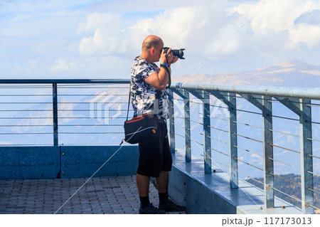 Travel photographer man with professional camera taking photos of  on a top of Tahtali mountain near Kemer, Antalya Province in Turkey 117173013