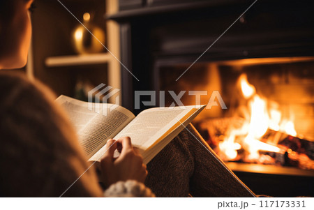 Woman reading a book by the fireplace in a cozy warm home close up, autumn vibe concept 117173331