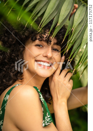 Smiling female model standing with fresh exotic foliage in the background Smiling female model standing with fresh exotic foliage in the background 117173752