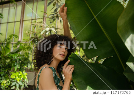 Adorable woman with dark curly hair on background of green leaves Adorable woman with dark curly hair on background of green leaves 117173766