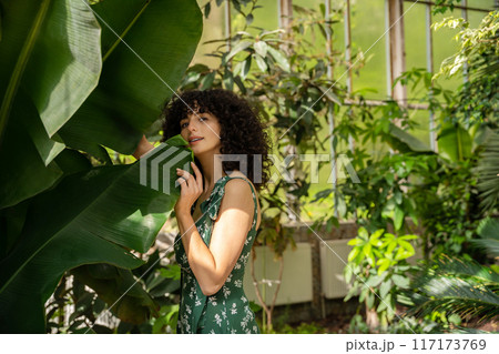Brunette woman with dark curly hair and green leaves in the background 117173769