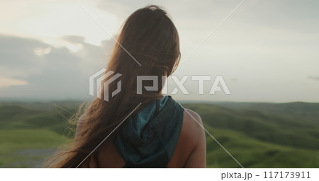 Woman enjoy green hills landscape at sunset. Long hair brunette girl looking on beautiful nature scene, hair blowing in wind. Freedom, happiness lifestyle. Travel, tourism, holiday. Slow 4k Woman enjoy green hills landscape at sunset. Long hair brunette girl looking on beautiful nature scene, hair blowing in wind. Freedom, happiness lifestyle. Travel, tourism, holiday. Slow 4k 117173911