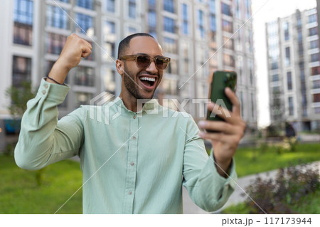 Man scrolling online using cellphone reading news in internet walking on big city urban street outside 117173944