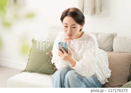 リビングでスマホを見るミドル女性 117176375