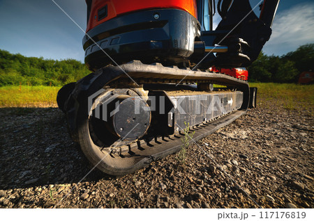 Close-up of rubber tracks of a small excavator outdoors surrounded by grass and greenery on a sunny day Close-up of rubber tracks of a small excavator outdoors surrounded by grass and greenery on a sunny day 117176819