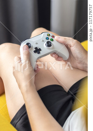 The woman is holding a white jostic, joystick, navigation key, cursor buttons, navigation control. She plays the game on the console. Close up vertical The woman is holding a white jostic, joystick, navigation key, cursor buttons, navigation control. She plays the game on the console. Close up vertical 117179757