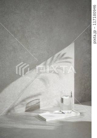 A gray-toned tile background with various props with sunlight coming through the window. 117180946