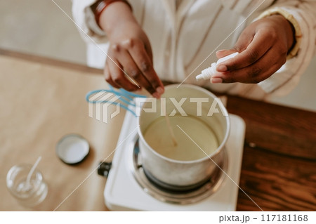 Hands carefully pouring liquid into container while standing at workspace. Surroundings include various crafting tools, hinting at meticulous, creative process Hands carefully pouring liquid into container while standing at workspace. Surroundings include various crafting tools, hinting at meticulous, creative process 117181168
