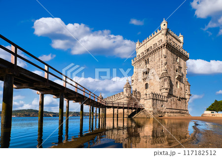 Belem tower and wooden bridge to it, Lisbon, Portugal at blue summer day sky with clouds. Medieval fort on Tagus river in late Gothic or Manueline style, UNESCO world heritage site, Age of Discoveries 117182512