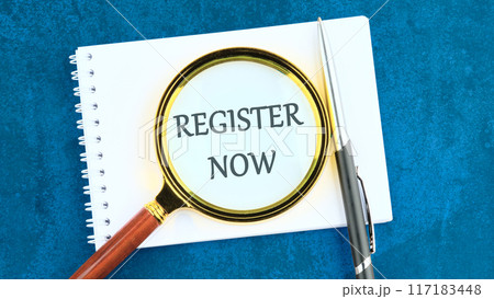 REGISTER NOW words written through the lens of a magnifying glass in a notebook and an abstract background 117183448