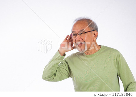 Portrait Asian old man with glasses and a beard listening to sound something, possibly engaged in conversation or trying to understand a message, hand on ear hearing a rumor isolated white background 117185846