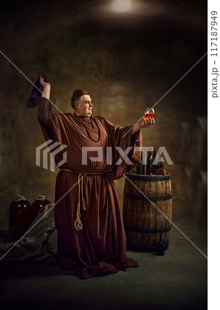 Medieval monk joyfully raising glass of ale, cognac or beer, showing rich tradition and celebration of Oktoberfest in monastic setting. Medieval monk joyfully raising glass of ale, cognac or beer, showing rich tradition and celebration of Oktoberfest in monastic setting. 117187949