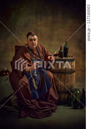 Rich tradition of craftsmanship of abbey ale production. Medieval monk sitting in dark vintage looking space with barrel of beer and wine. Rich tradition of craftsmanship of abbey ale production. Medieval monk sitting in dark vintage looking space with barrel of beer and wine. 117188003