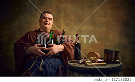 Delightful man, monk holding various bottles filled with beer, ale, and wine against vintage background. Brewing organic beverages 117188029