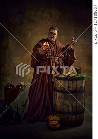 Man, medieval monk in period robe. holding glass of beer, ale against vintage dark textured background. Time-honored practices of monastic brewing. Man, medieval monk in period robe. holding glass of beer, ale against vintage dark textured background. Time-honored practices of monastic brewing. 117188057