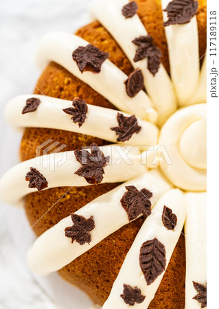 Icing the pumpkin bundt cake with cream cheese frosting and decorating it with chocolate leaves. Icing the pumpkin bundt cake with cream cheese frosting and decorating it with chocolate leaves. 117189118