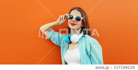 Summer portrait happy modern young woman listening to music with headphones on orange background 117189229