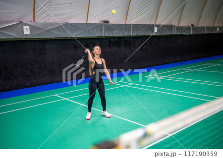 Sports young woman with racket and shuttlecock is exercising, playing in badminton on inside court 117190359