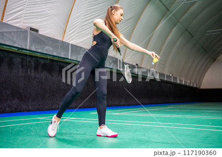 Sports young woman with racket and shuttlecock is practicing serve before playing in badminton on inside court 117190360