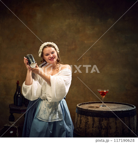 Medieval woman, bar tender, in traditional attire shaking cocktail mixer, surrounded by bottles and filled glass on rustic barrel. 117190628