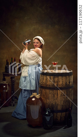Medieval woman in traditional attire shaking cocktail mixer, surrounded by bottles and filled glass on rustic barrel, as bar counter. Medieval woman in traditional attire shaking cocktail mixer, surrounded by bottles and filled glass on rustic barrel, as bar counter. 117190632
