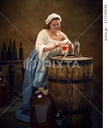 Medieval woman in traditional attire, preparing festive drink for celebration, serving alcohol cocktail, ant vintage bar counter in pub. Medieval woman in traditional attire, preparing festive drink for celebration, serving alcohol cocktail, ant vintage bar counter in pub. 117190656