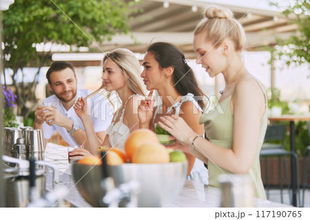 Friends, man and beautiful young women enjoying cocktails and friendly atmosphere at chic outdoor bar. Weekend vibes and refreshment Friends, man and beautiful young women enjoying cocktails and friendly atmosphere at chic outdoor bar. Weekend vibes and refreshment 117190765