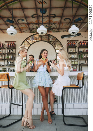 Friends meeting in modern bar, restaurant for relaxation and conversation. Three beautiful women enjoying cocktails and company 117190829