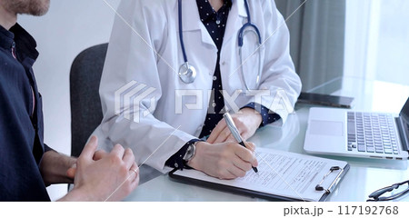 Doctor and patient are talking in clinic after usual health check up. Female physician is making notes awhile man is describing something. Medicine concept Doctor and patient are talking in clinic after usual health check up. Female physician is making notes awhile man is describing something. Medicine concept 117192768