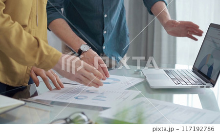 Business people, professionals analyzing financial charts and data on a desk while standing and using laptop computer in office 117192786