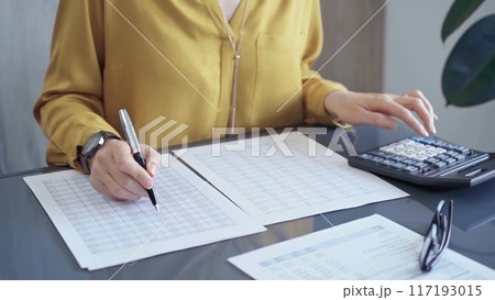 Professional business woman in yellow blouse is working on financial reports. Close-up of a woman's hands using calculator for audit or accounting 117193015