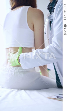 Doctor and patient. Physician wearing green medical gloves examining back of female patient in clinic. Orthopedics and medicine 117193023