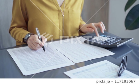 Professional business woman in yellow blouse is working on financial reports. Close-up of a woman's hands using calculator for audit or accounting 117193067