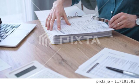 Businessman or auditor wearing green shirt is reviewing financial documents with magnifying glass. Business work process in bookkeeping office. Taxes Businessman or auditor wearing green shirt is reviewing financial documents with magnifying glass. Business work process in bookkeeping office. Taxes 117193393