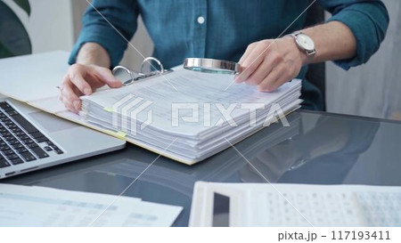 Businessman or professional auditor is analyzing data sheets. Close-up of an bookkeeper's hand with magnifying glass inspecting financial reports. Business audit and taxes Businessman or professional auditor is analyzing data sheets. Close-up of an bookkeeper's hand with magnifying glass inspecting financial reports. Business audit and taxes 117193411
