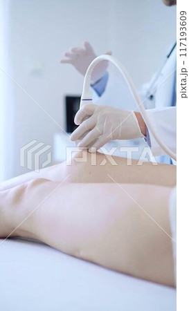 Male doctor with white medical gloves using ultrasound equipment on the knee of a female patient. The results on a monitor in the background. Medicine concept 117193609