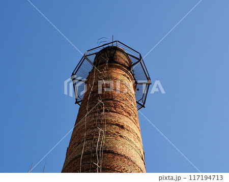 Industrial tower or pipe with observation balcony. Smokestacks with ladder or stairs. Tall brick chimneys above abandoned boiler building for venting smoke, combustion byproducts from factory heating Industrial tower or pipe with observation balcony. Smokestacks with ladder or stairs. Tall brick chimneys above abandoned boiler building for venting smoke, combustion byproducts from factory heating 117194713