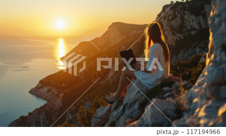 Woman Working on Laptop During Sunset on Rocky Cliff 117194966
