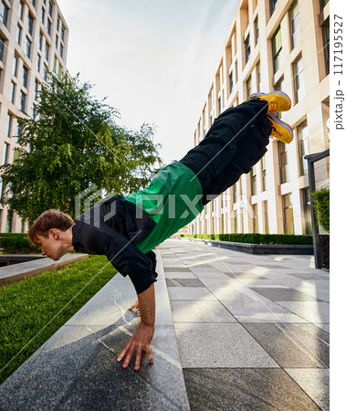 Showcasing impressive athleticism, parkrunner balances on hands , framed by towering city buildings, embodying spirit of parkrun. 117195527