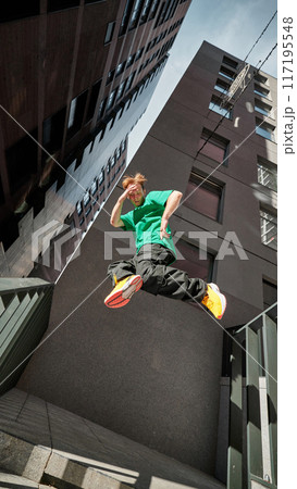Parkrunner flips high, framed by modern city buildings, capturing exhilarating spirit and dynamic energy of modern life. 117195548