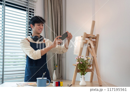Young Artist Taking a Photo of His Artwork in a Modern Studio with Natural Light and Creative Ambiance 117195561