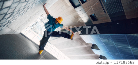 Creative photo. Dancer in yellow bucket hat and blue shirt performs handstand against modern urban backdrop. Strength and style. 117195568