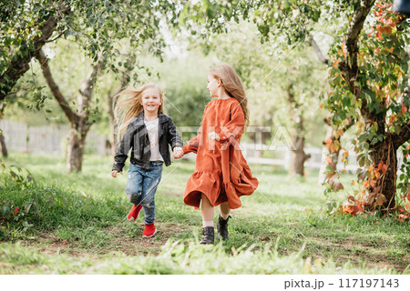 Children whirling, dancing plays on meadow. Girls having fun. Cute little longhair blonde girl dancing at sunset park. Selective focus. innocence and happiness of childhood 117197143