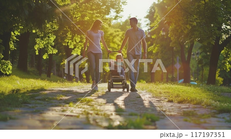 young couple walks hand-in-hand with their baby in a stroller on a sunny day, enjoying a leisurely walk through a lush park. 117197351