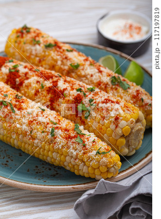 Delicious Mexican dish Elotes corn cob covered in spices and cheese 117197819